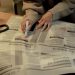 An adult woman marks job listings in a newspaper while sitting indoors, highlighting job search activity.